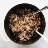 Overhead image of two forks shredding carnitas in a dutch oven.