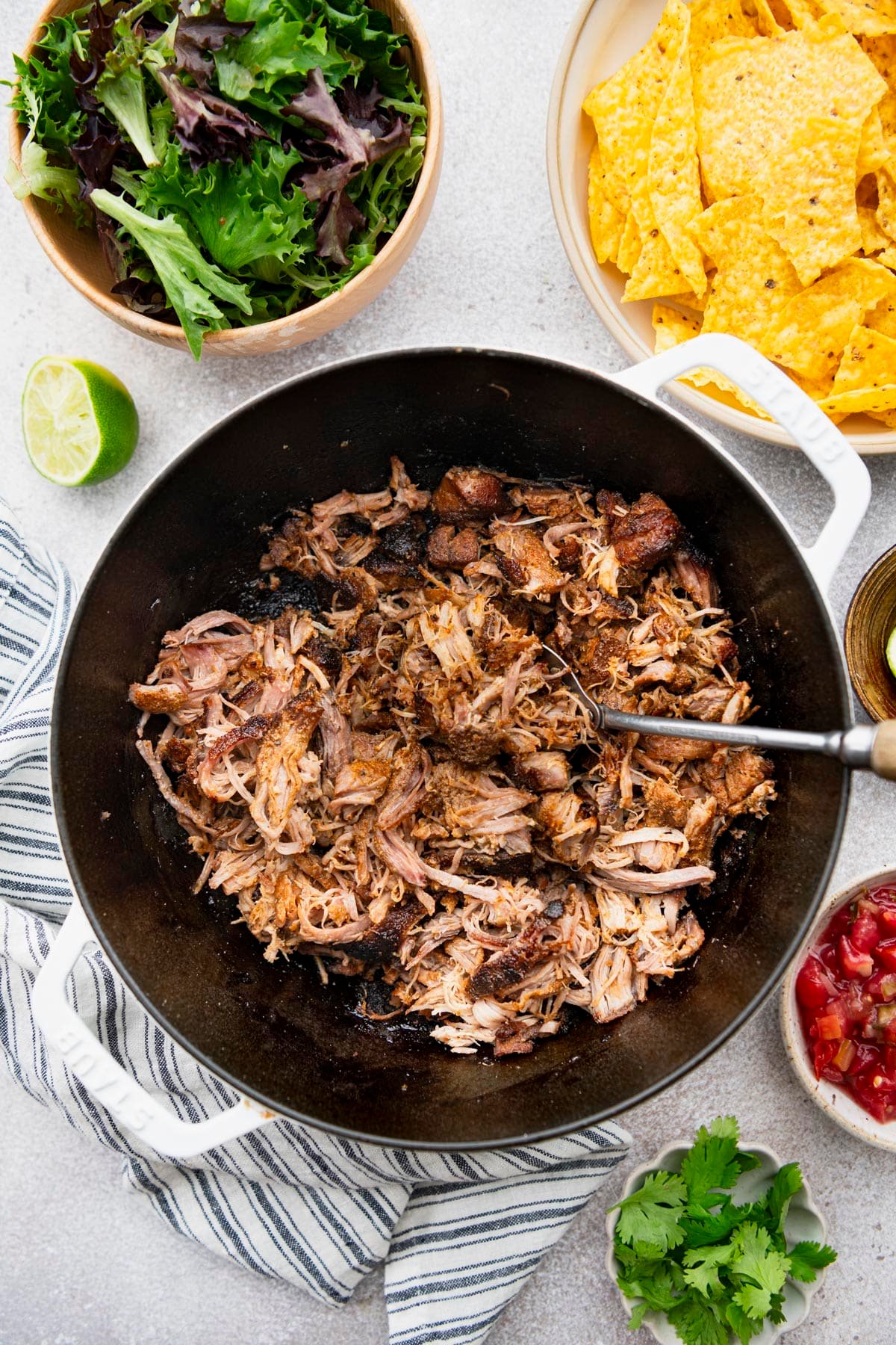 Dutch oven Mexican pulled pork carnitas on a white table with all of the toppings.