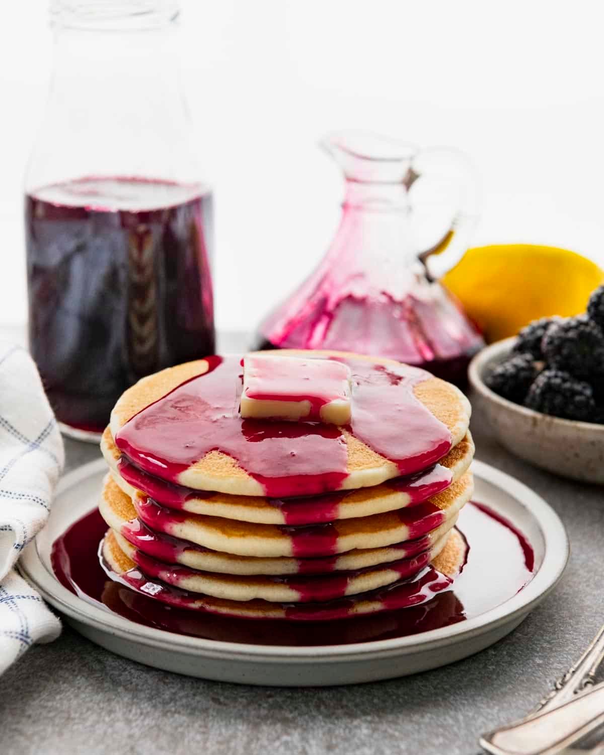 Side shot of pancakes with blackberry syrup on a breakfast table.
