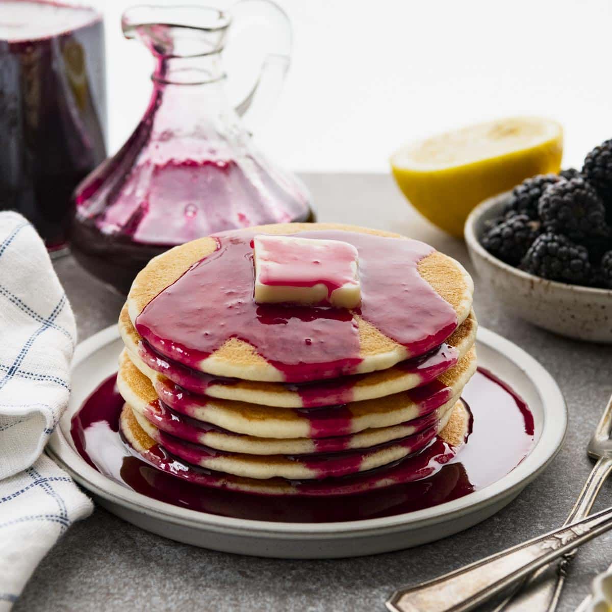 Square side shot of a stack of pancakes with blackberry syrup.