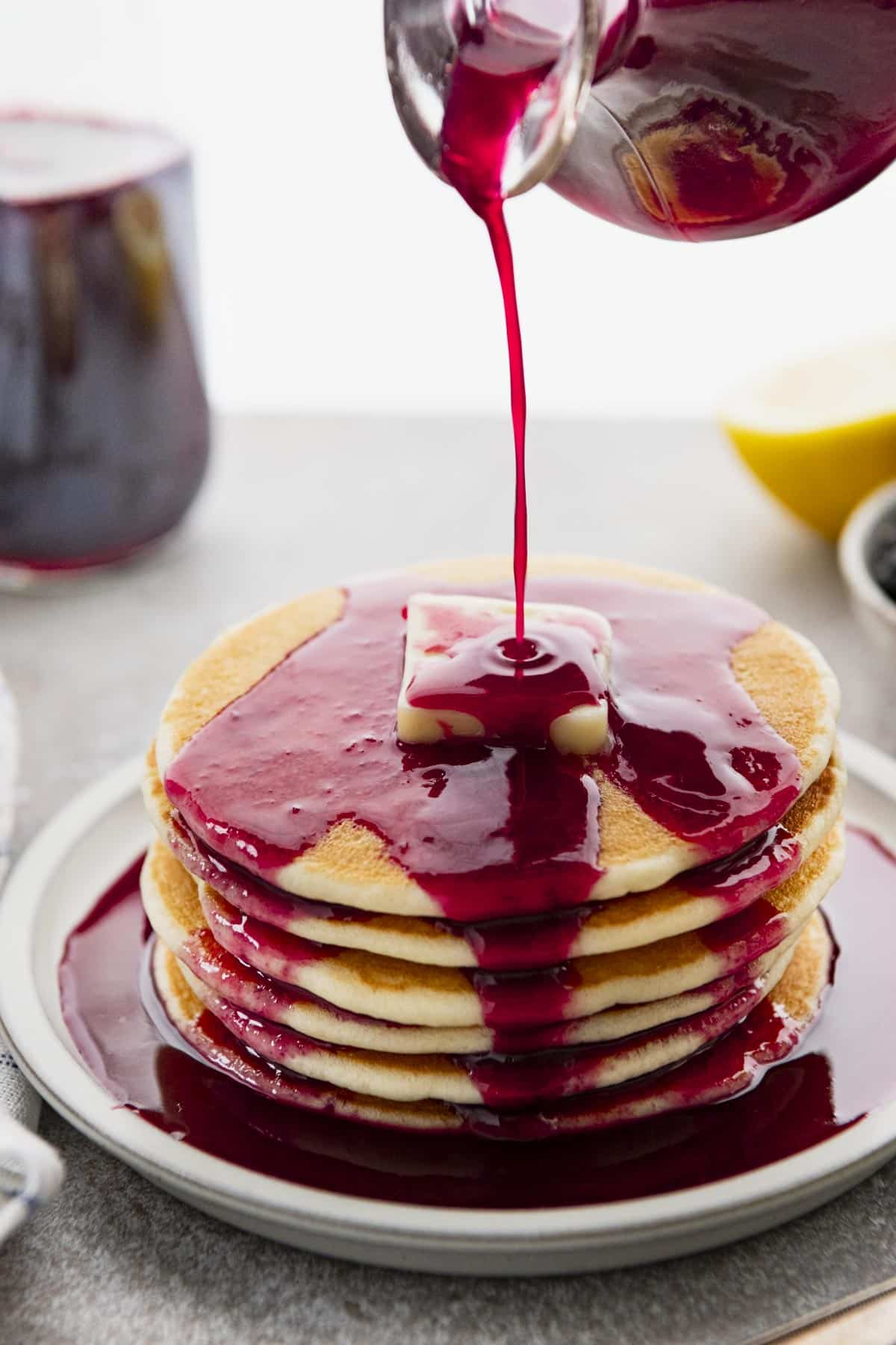 Front shot of pouring blackberry syrup on a stack of pancakes.
