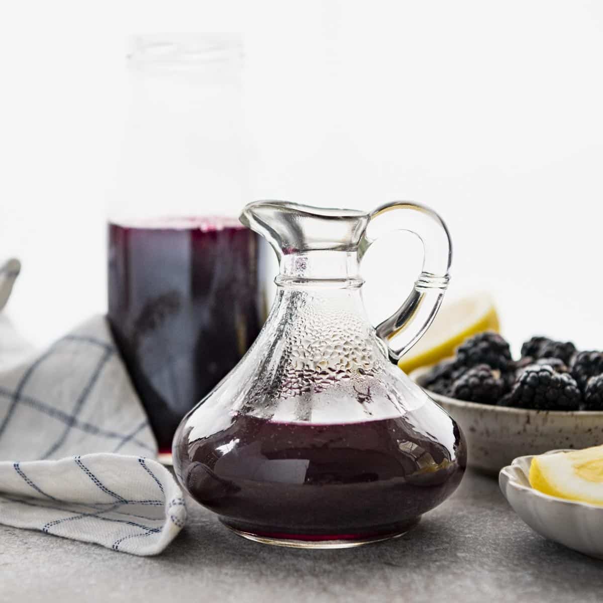 Square side shot of blackberry syrup recipe stored in a glass pitcher.