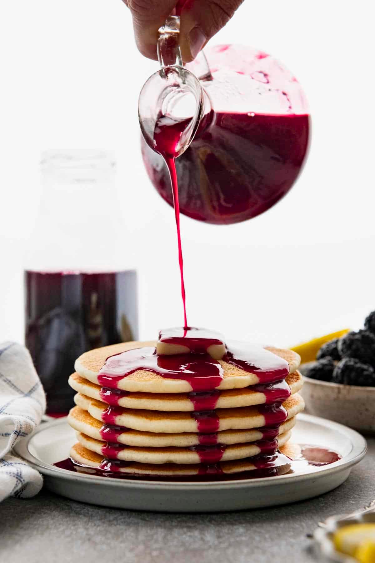 Pouring the best blackberry syrup recipe on a plate of pancakes.