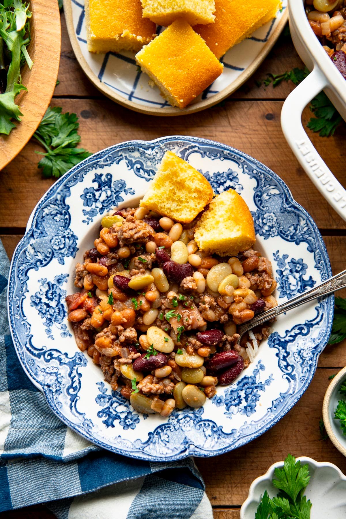 Overhead image of grandma's calico beans recipe on a wooden table with a side salad and cornbread.