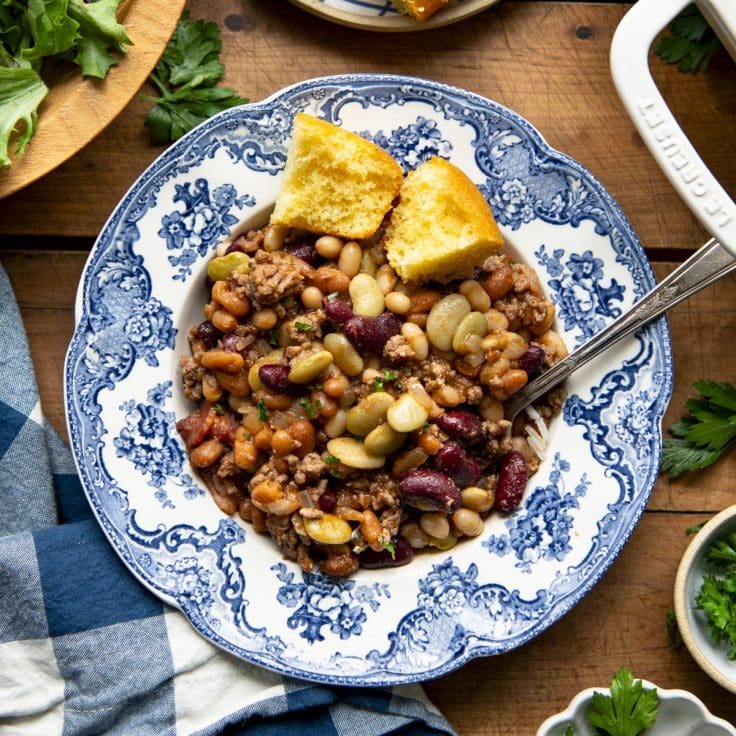 Square overhead shot of calico beans in a blue and white bowl with a side of cornbread.