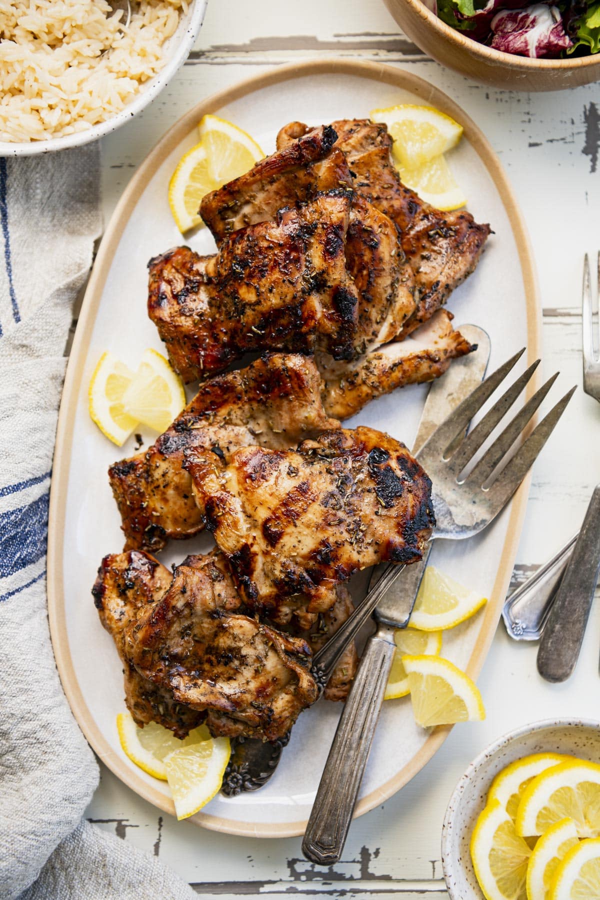 Overhead image of a white tray full of beautiful grilled marinated chicken thighs with fresh lemons.