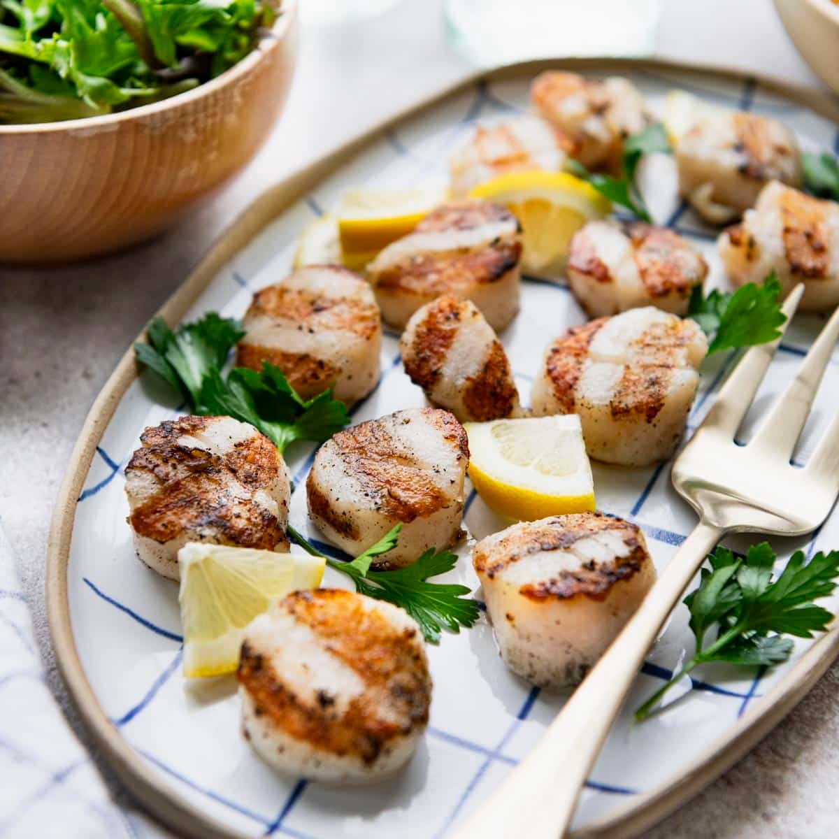 Square front shot of grilled scallops on a serving platter with lemon and parsley.