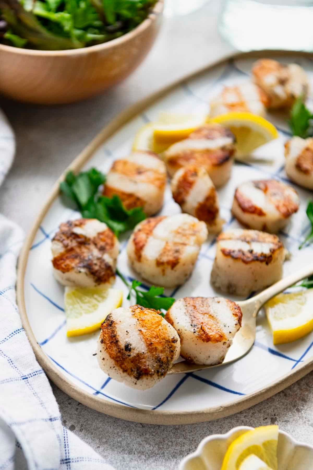 The best grilled scallops recipe served with lemon and parsley on a platter.