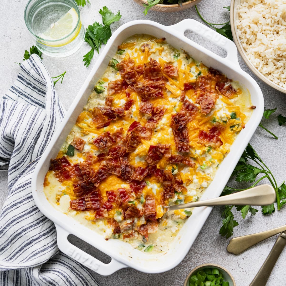 Square overhead shot of jalapeno popper chicken casserole in a white dish with crispy bacon on top.