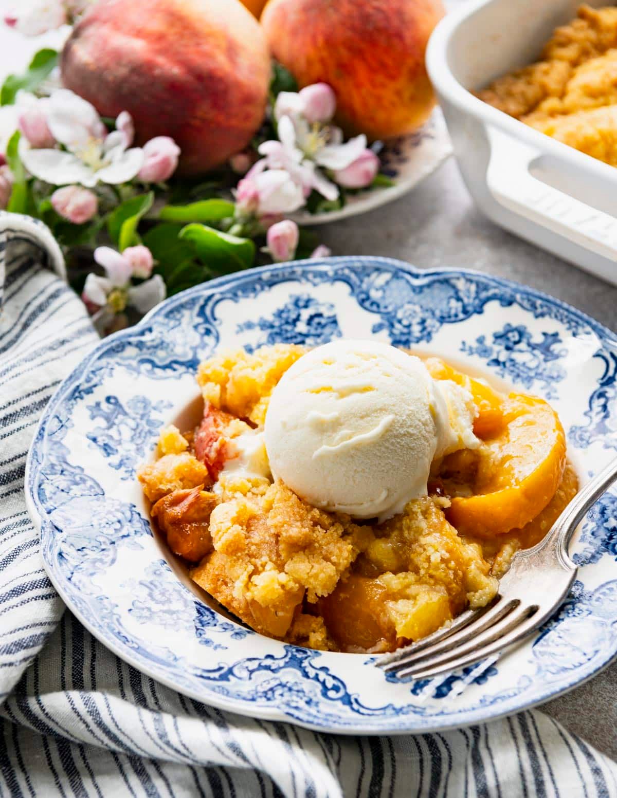 Front shot of a blue and white bowl full of Jiffy peach cobbler with ice cream on top.