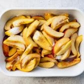 Sliced peaches and sugar in a white baking dish.