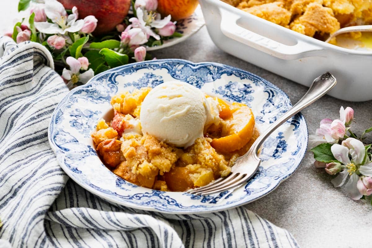 Horizontal side shot of a blue and white bowl full of the best southern peach cobbler recipe with ice cream on top.