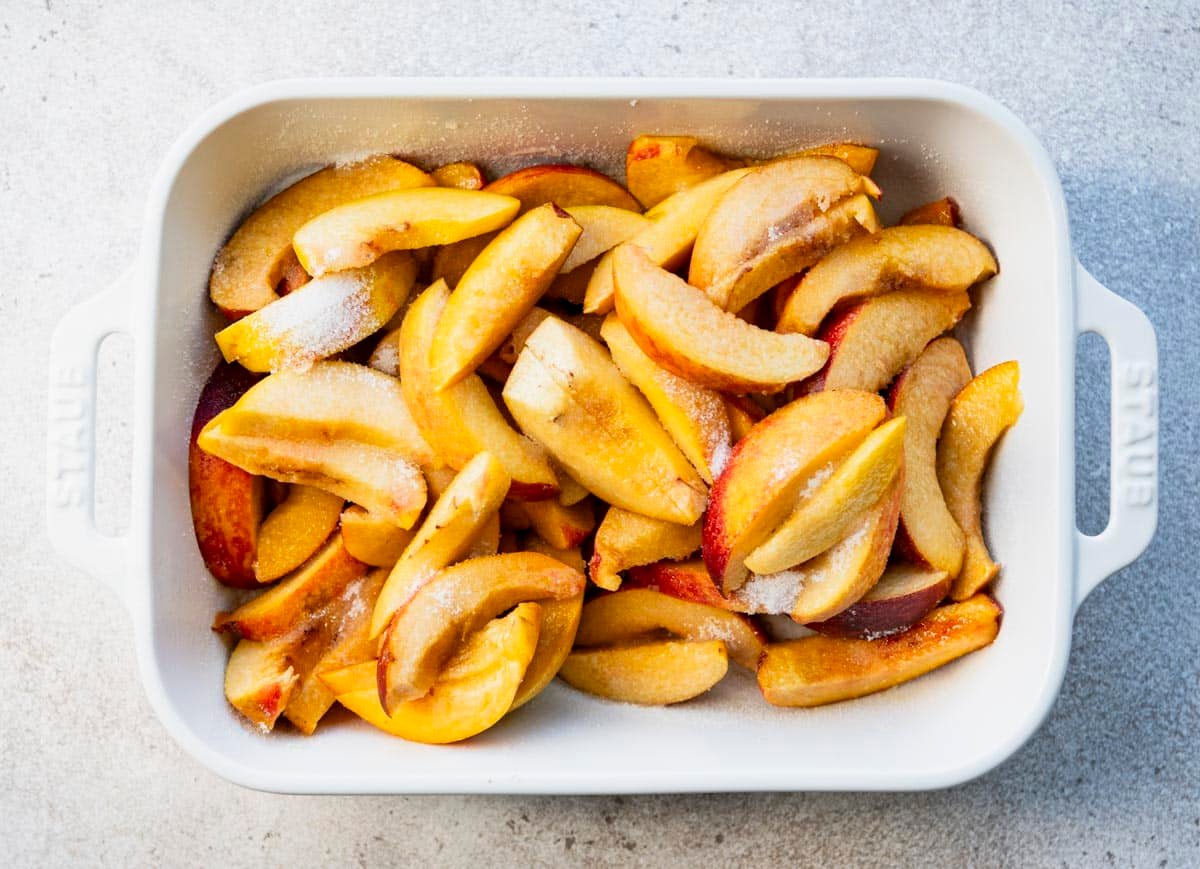 Sliced peaches and sugar in a white baking dish.