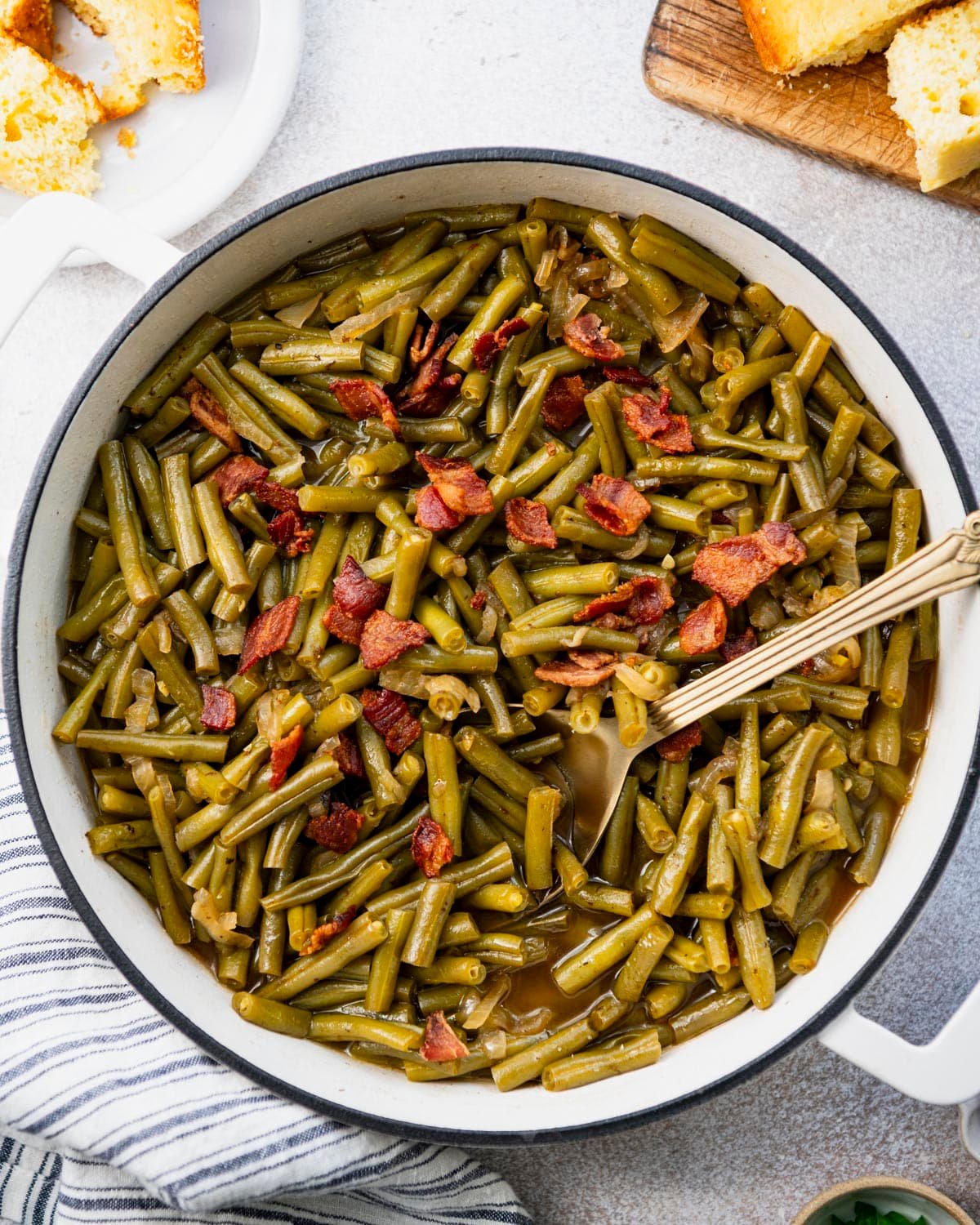 Close overhead image of Southern green beans in a white cast iron pot with a side of cornbread.