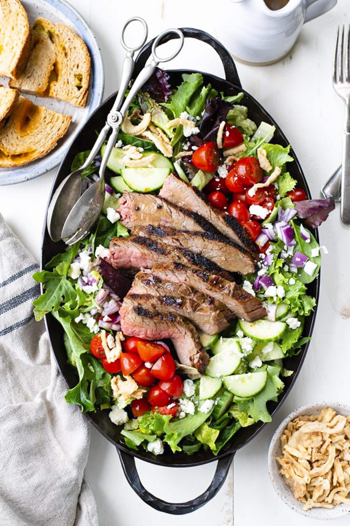 Overhead shot of steak salad on a white table with a side of homemade bread.