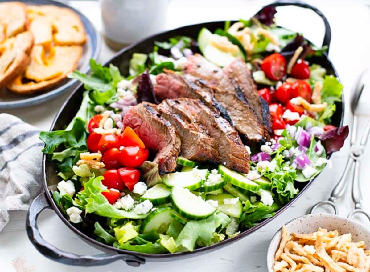 Horizontal side shot of steak salad on a white table.