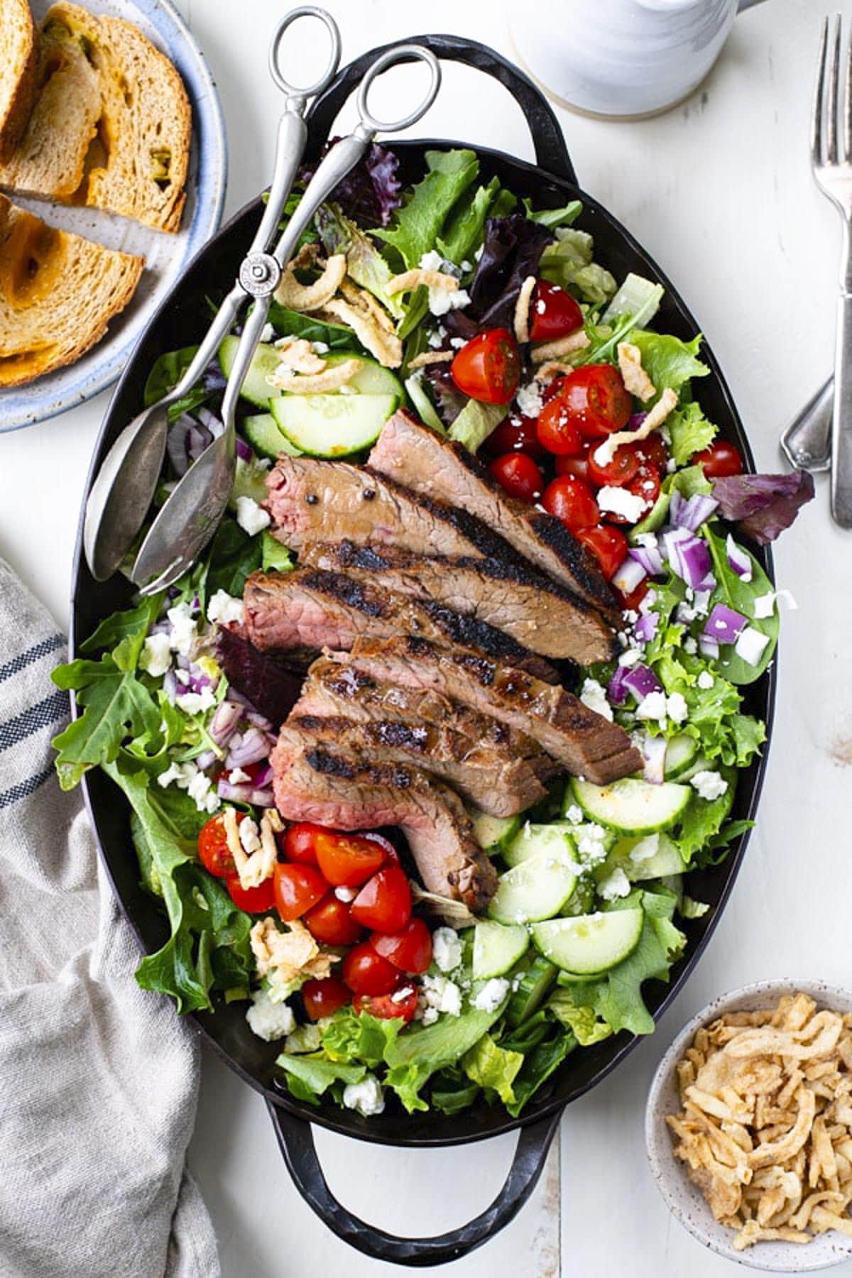 Overhead shot of sliced flank steak and homemade dressing on top of a steak salad.