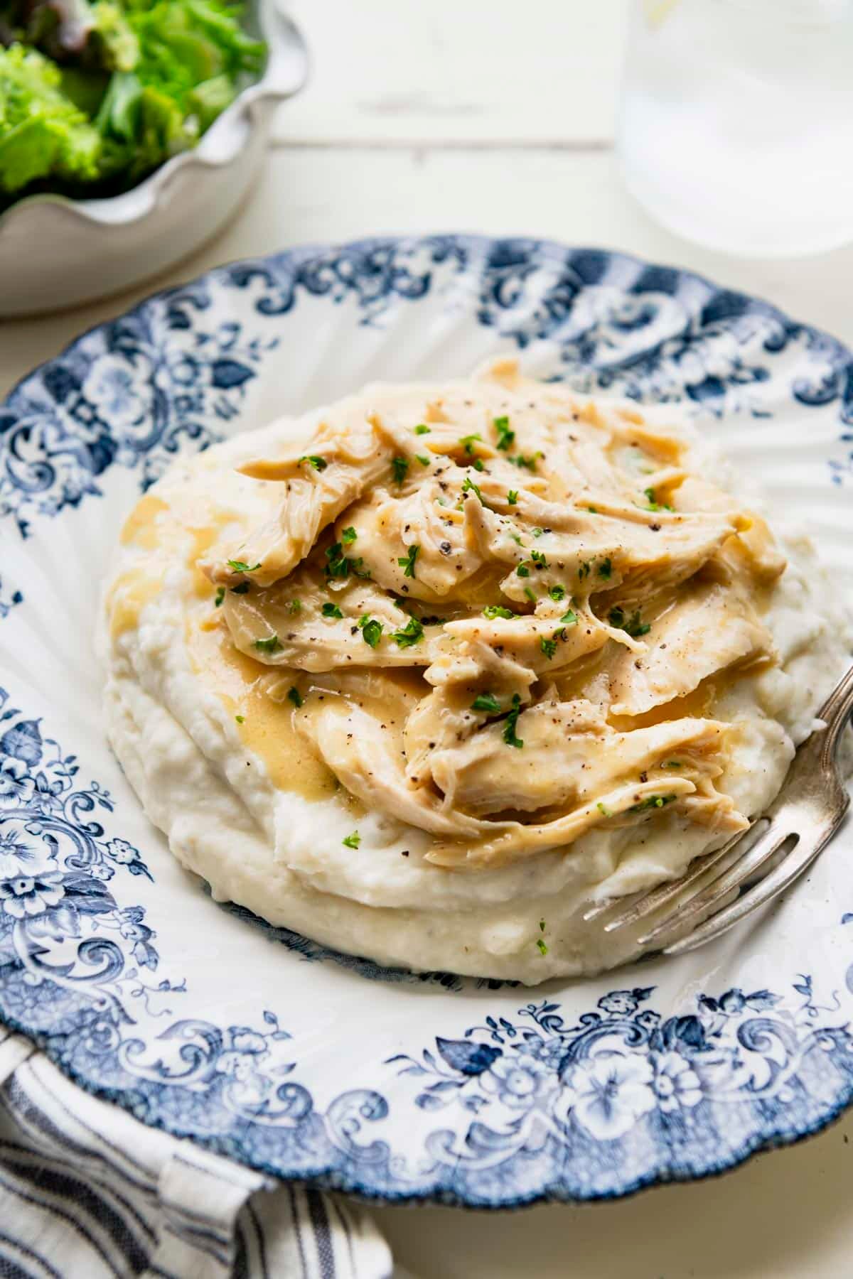 Close up front shot of crock pot chicken with gravy on a bed of mashed potatoes.