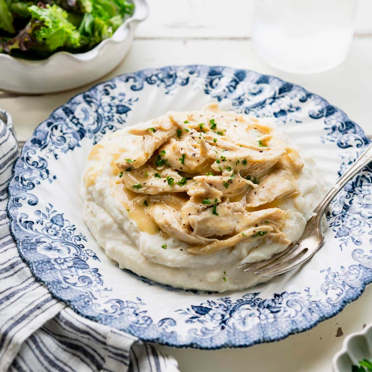 Square side shot of a plate of 3 ingredient crockpot chicken and gravy on top of mashed potatoes.