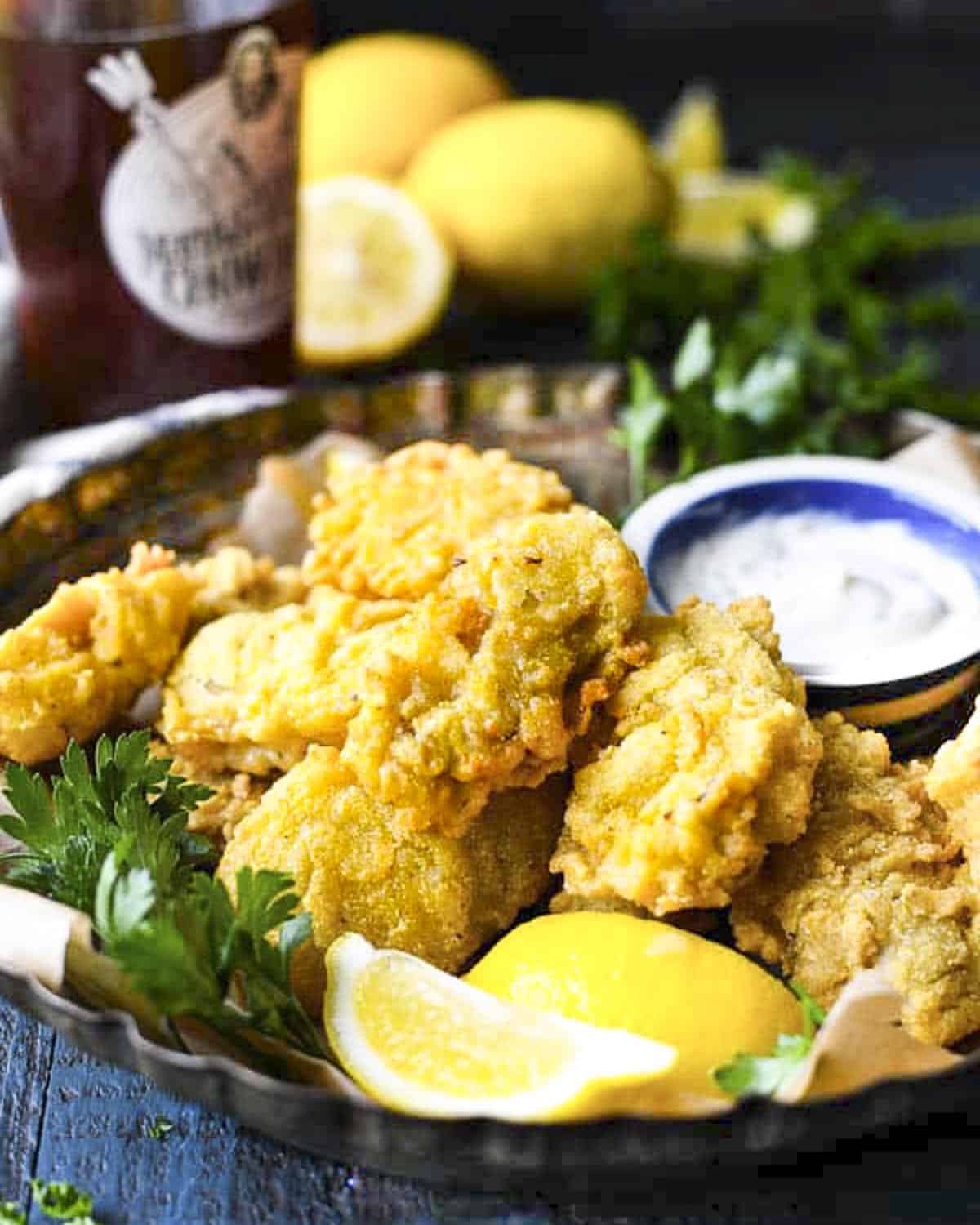 Front shot of a tray of deep fried oysters with lemons and a cold beer in the background.