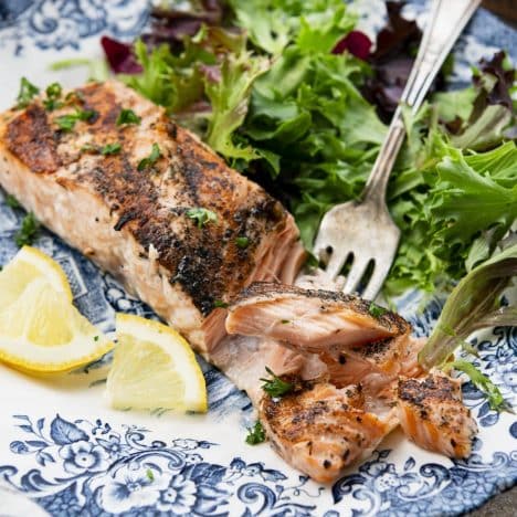 Square side shot of a plate of grilled salmon with salad and lemon.