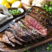 Square side shot of a marinated and grilled London broil steak on a wooden cutting board.