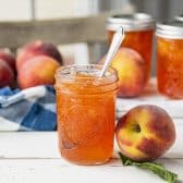 Horizontal side shot of jars of fresh peach jam on a white farmhouse table.