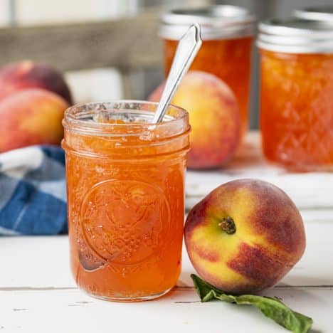 Square side shot of jars of peach jam on a white rustic table.