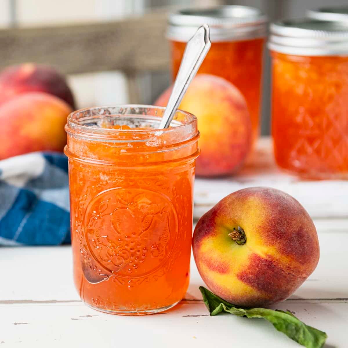 Square side shot of jars of peach jam on a white rustic table.