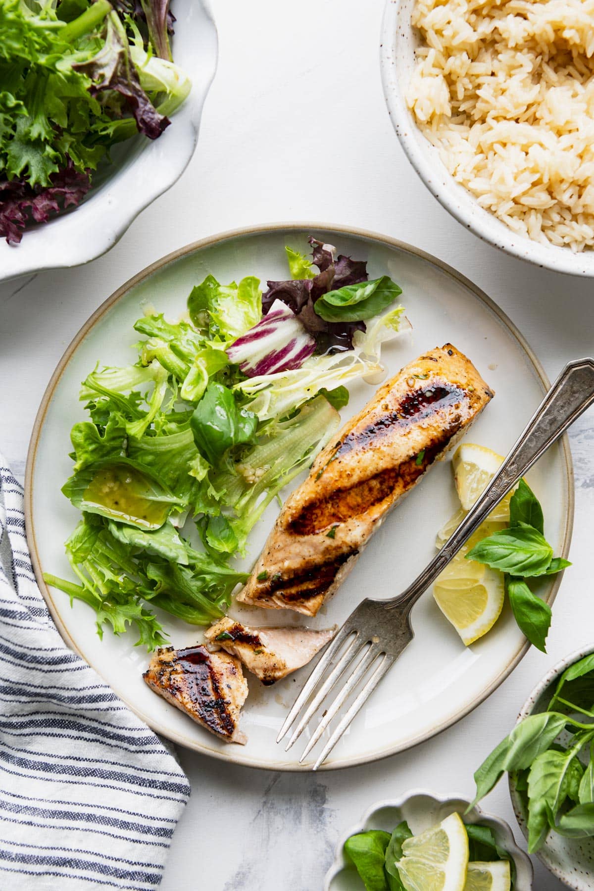 Overhead shot of marinated grilled salmon on a white table with salad and rice.