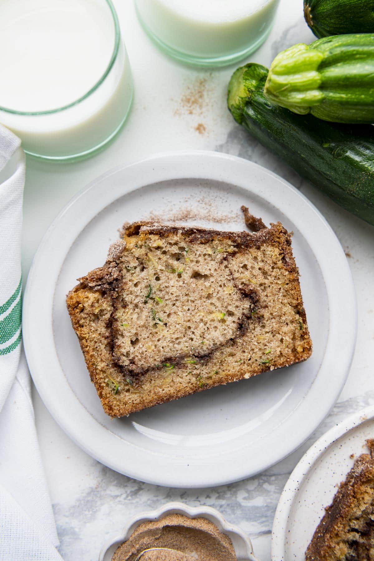 Overhead image of a slice of snickerdoodle zucchini bread on a white table with a glass of milk.