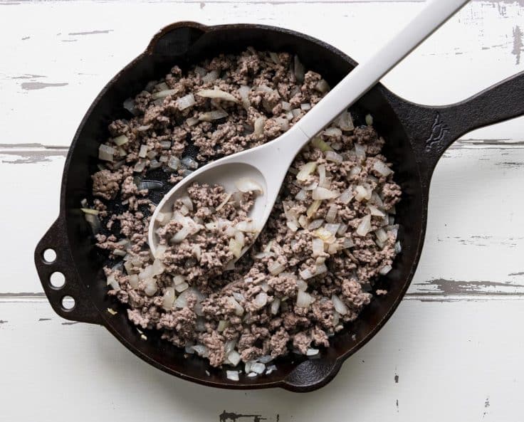 Ground beef and onion in a cast iron skillet.