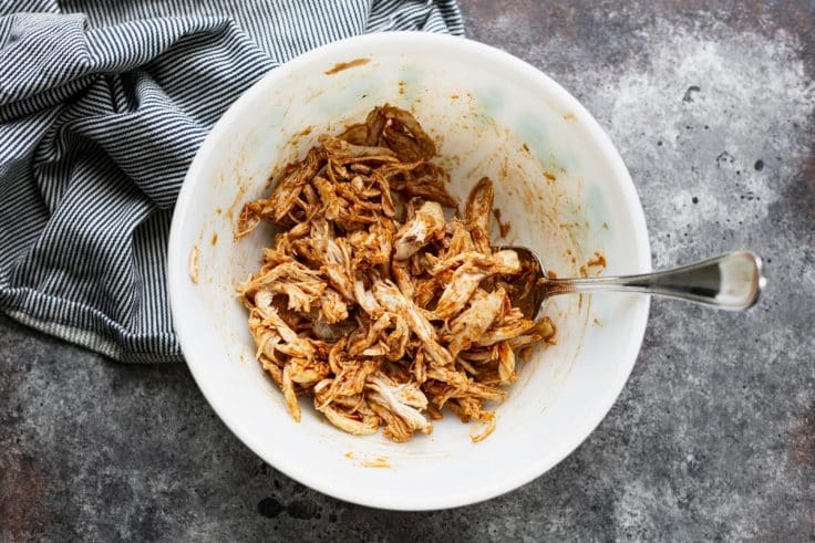 Shredded rotisserie chicken tossed with bbq sauce in a bowl.