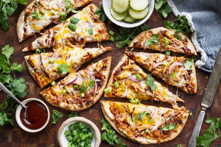 Horizontal overhead image of flatbread bbq chicken pizza sliced on a wooden cutting board.