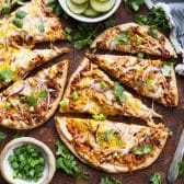 Square overhead image of a flatbread bbq chicken pizza on a cutting board with fresh cilantro and cucumber salad on the side.