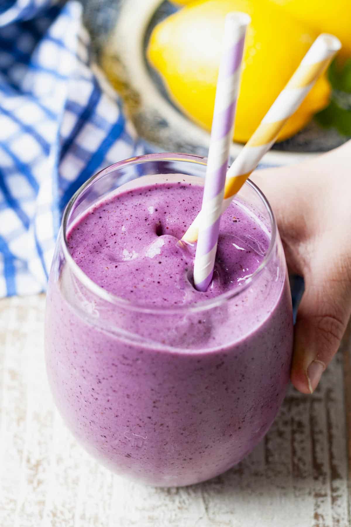 Child's hand holding a glass of blueberry banana smoothie.