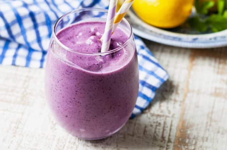 Horizontal shot of a banana blueberry smoothie on a white table.