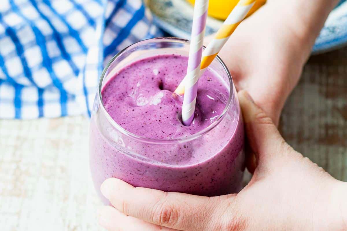 Horizontal image of a child's hands holding a blueberry banana smoothie.
