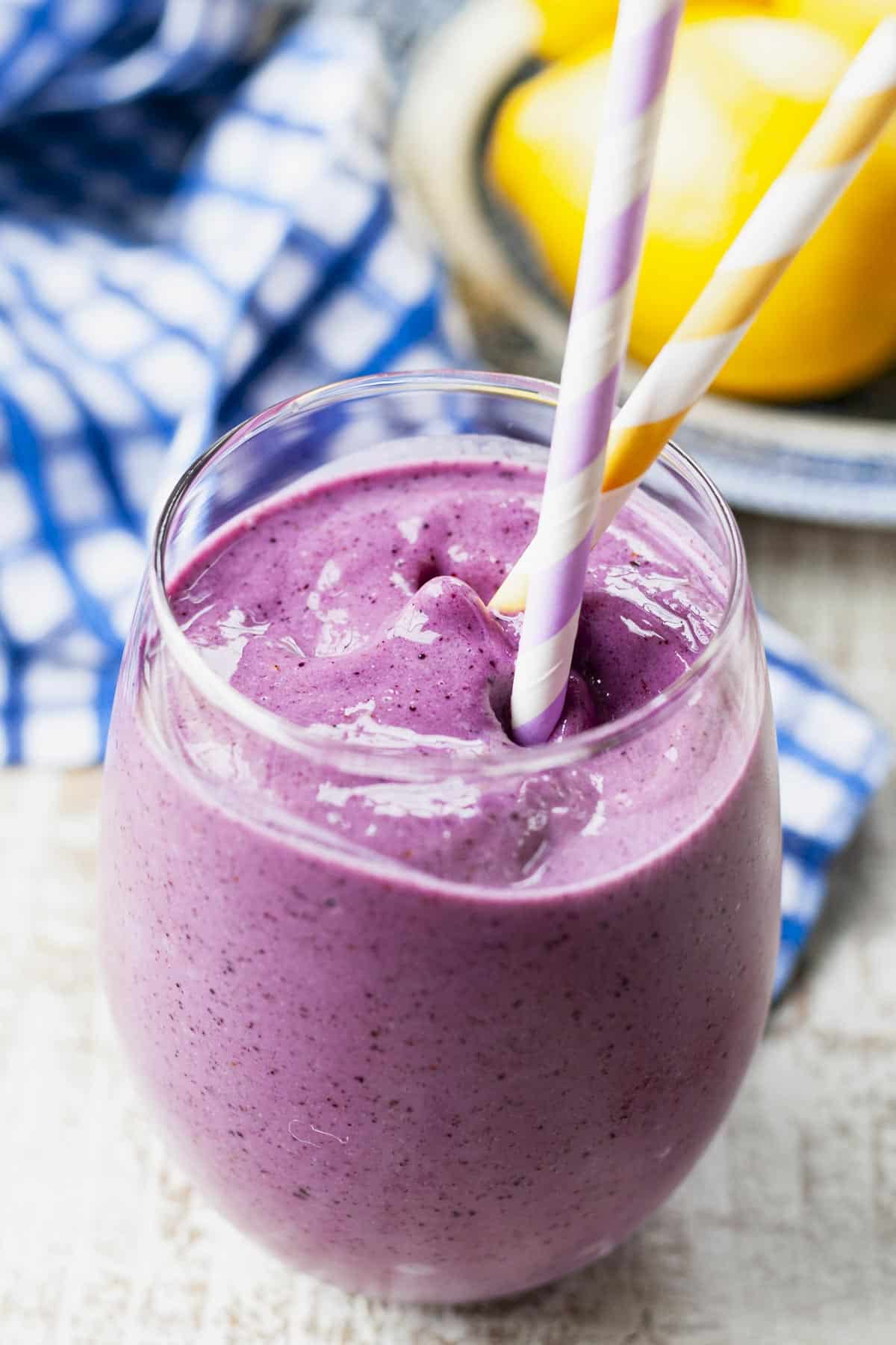 Close up shot of two straws in a blueberry banana smoothie with greek yogurt and milk.