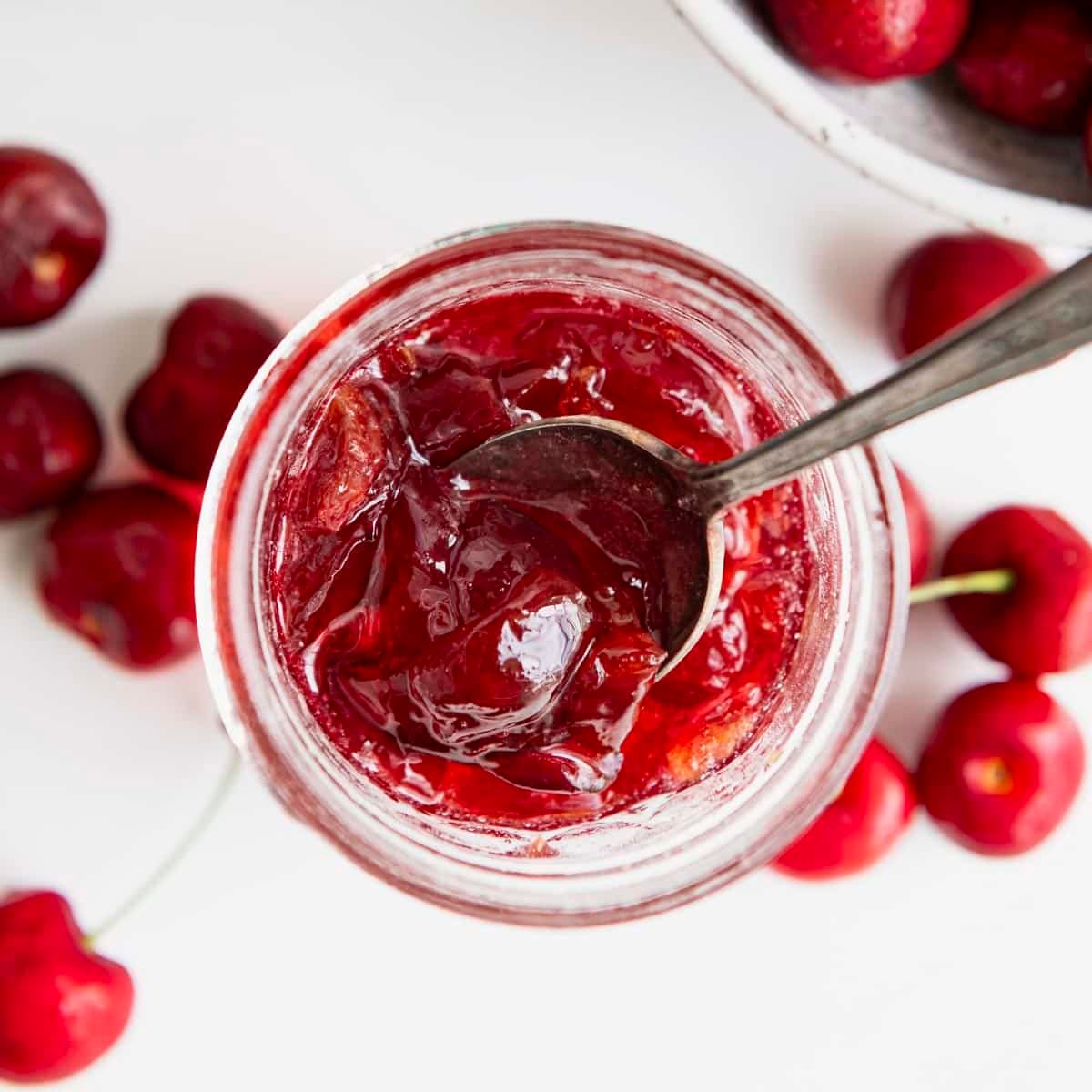 Square overhead shot of the best cherry jam recipe in a glass mason jar.