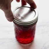Screwing a lid on a mason jar full of homemade cherry jam.