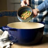 Adding frozen vegetables to a cast iron Dutch oven.