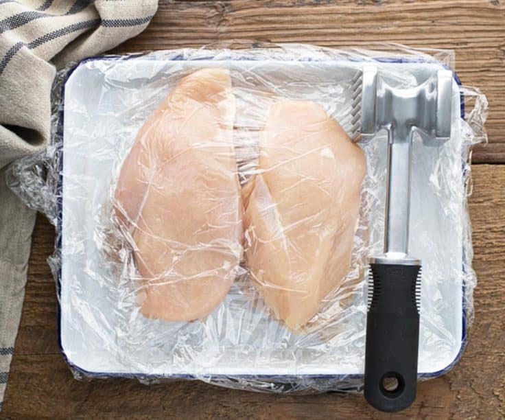 Pounding boneless skinless chicken breast on a tray.