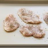 Chicken cutlets on a rimmed baking sheet with Italian seasoning.