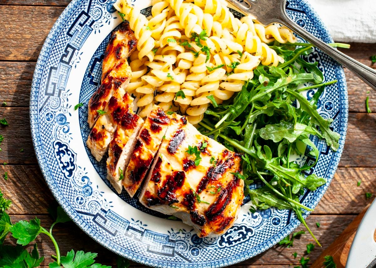 Horizontal overhead image of a blue and white plate full of grilled italian dressing chicken with a side of pasta and salad.