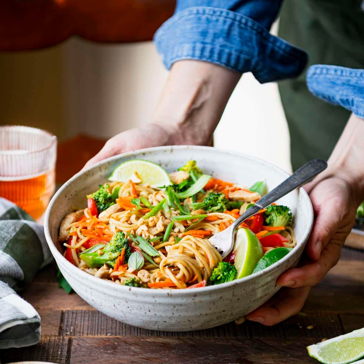 Square side shot of hands serving an easy chicken lo mein recipe in a bowl.