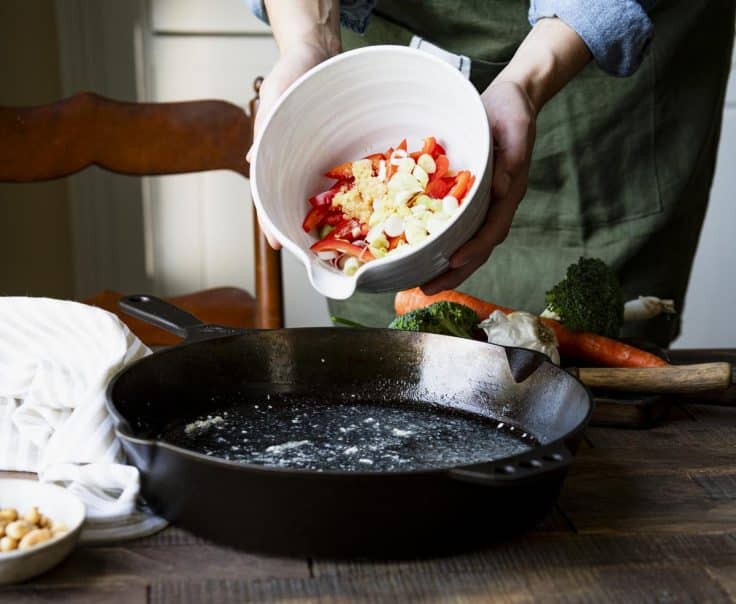 Adding vegetables to a cast iron skillet.