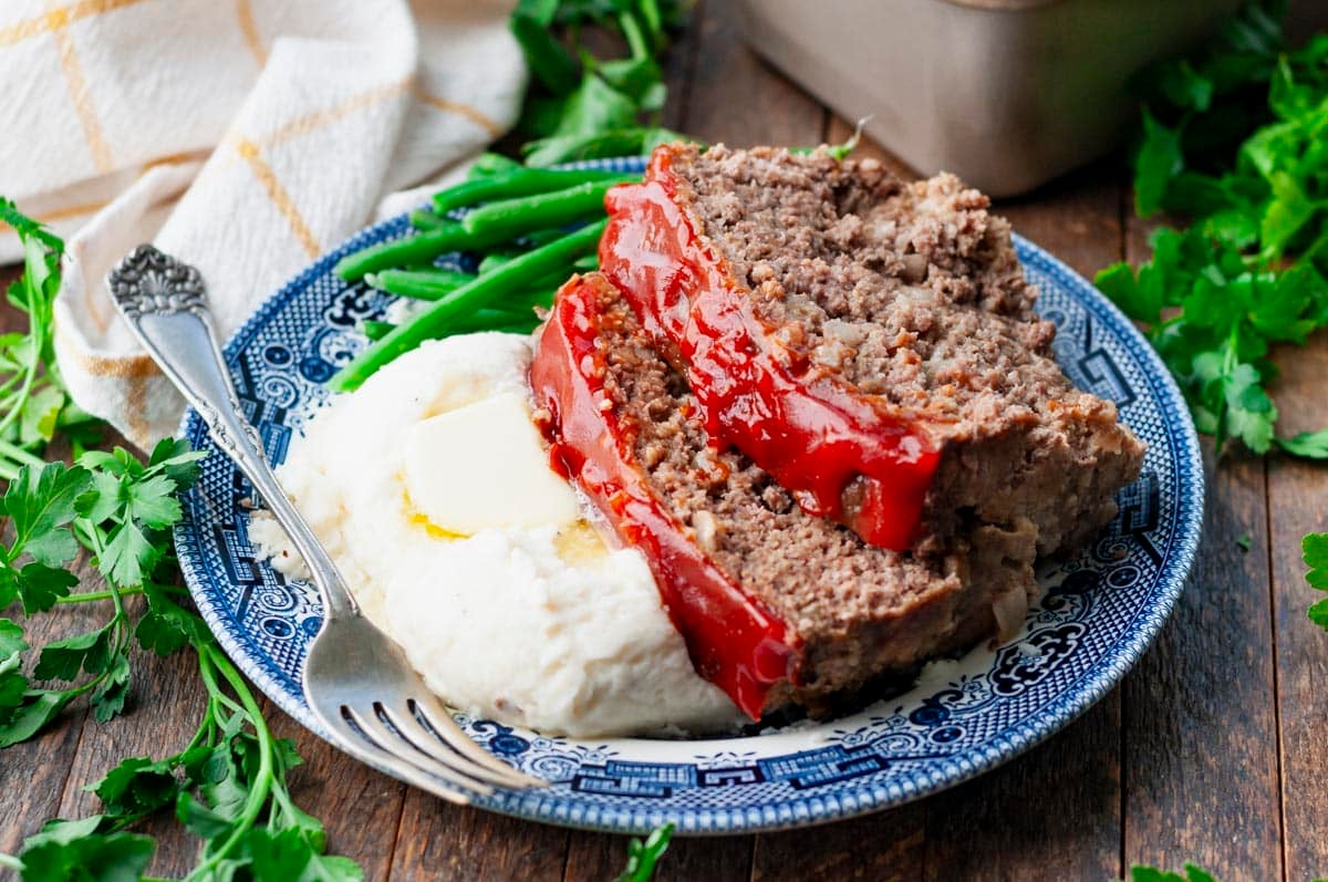 Horizontal side shot of a plate of the best meatloaf recipe with oatmeal served with mashed potatoes and green beans on the side.