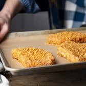 Breaded pork chops on a baking sheet before baking in the oven.