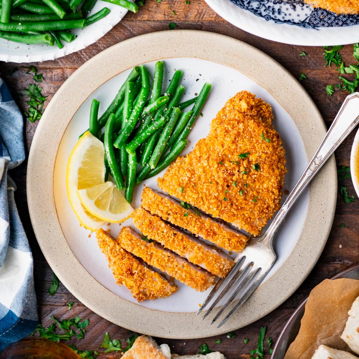 Square overhead shot of baked breaded pork chops on a plate with green beans.